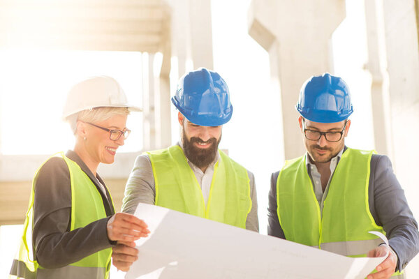 Satisfied team looks at building plans, the team consists of one woman and two men, they seem satisfied.