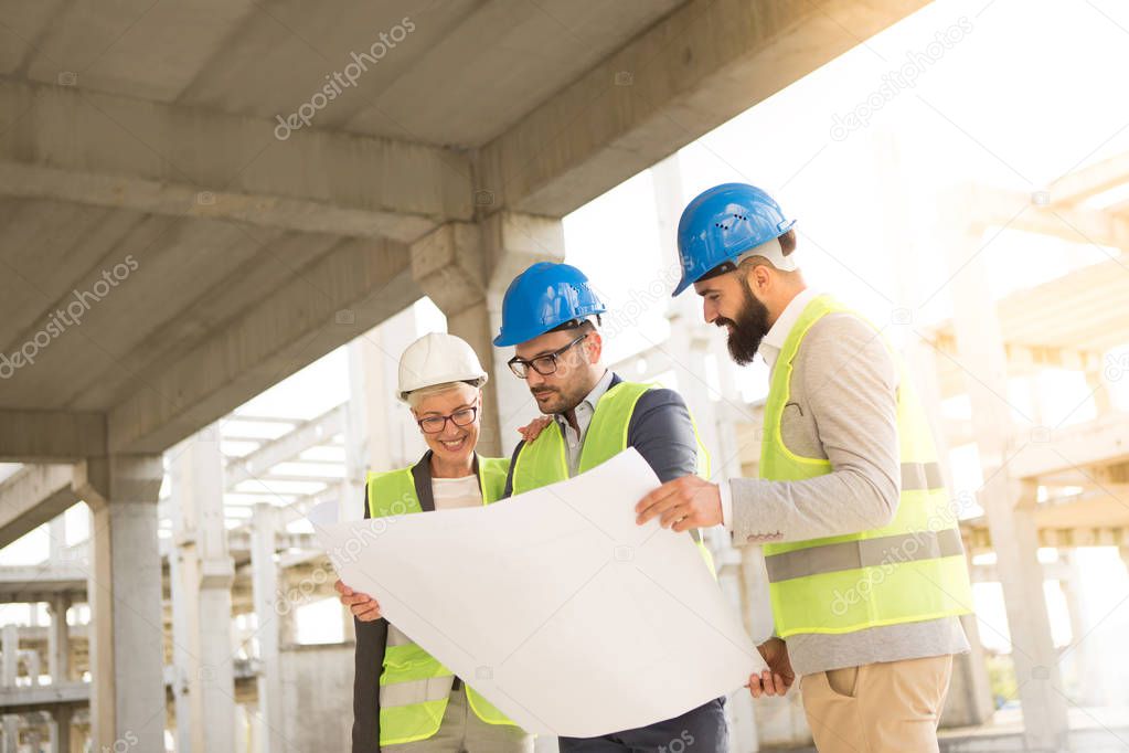 Satisfied team looks at building plans, the team consists of one woman and two men, they seem satisfied.
