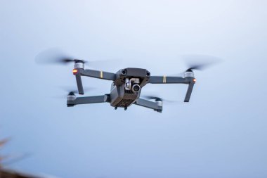 Modern, küçük, katlanabilir gri drone 'a odaklan. İnsansız hava aracı denizin kıyılarında uçar ve ateş eder. Arkasında mavi gökyüzünü görebilirsiniz..