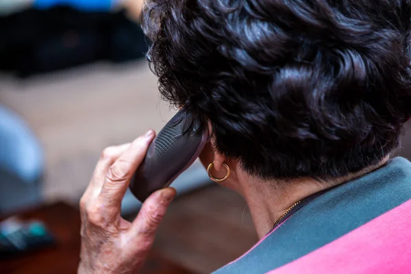 Seçici bir şekilde telefona odaklan. Telefon, kısa siyah saçlı, yaşlı bir kadının elinde ve şu anda konuşuyor. Resim arkadan çekilmiş..