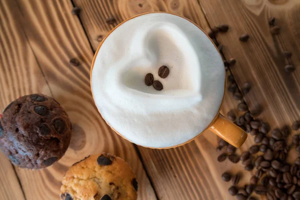 Чашка кофе с пеной в виде сердца с печеньем и кофейными зёрнами с кофемолкой на деревянном столе — стоковое фото