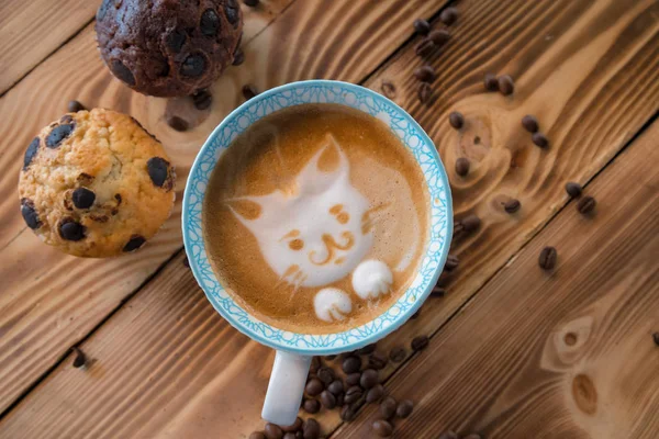 Cara de espuma de gato de café de arte latte en taza con granos de café dispersos y galletas en la mesa de madera vieja — Foto de Stock