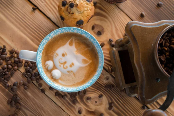 Cara de espuma de gato de café de arte latte en taza con granos de café dispersos y galletas en la mesa de madera vieja — Foto de Stock