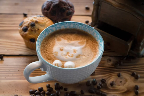 Cat foam face of latte art coffee in cup with scattered coffee beans and biscuits on old wooden table — Stock Photo, Image