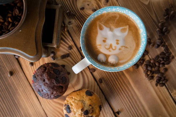 Cara de espuma de gato de café de arte latte en taza con granos de café dispersos y galletas en la mesa de madera vieja — Foto de Stock