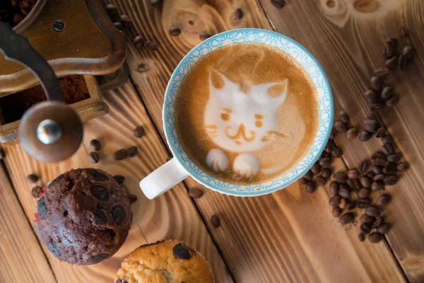 Кіт піни обличчя латте художньої кави в чашці з розкиданими кавовими зернами і печивом на старому дерев'яному столі — стокове фото