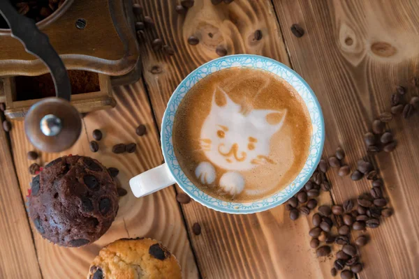 Cat foam face of latte art coffee in cup with scattered coffee beans and biscuits on old wooden table — Stock Photo, Image