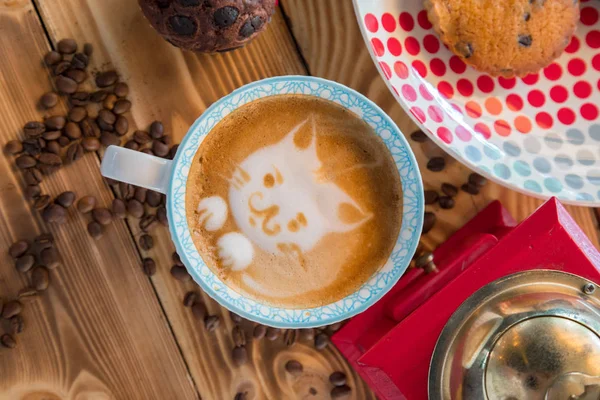 Molino de café rojo, taza de café con leche con un gato pintado en espuma de leche y galletas en una mesa de madera vieja . — Foto de Stock