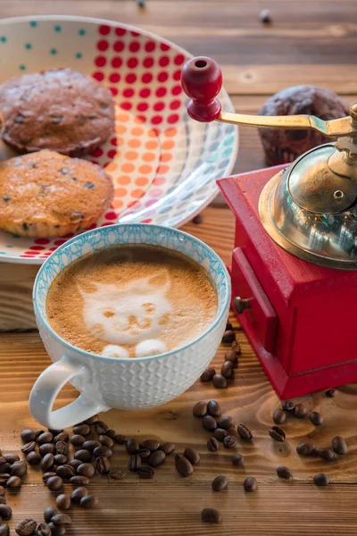 Red coffee mill, cup latte with a painted cat on milk foam and biscuits on a old wooden table. — Stock Photo, Image