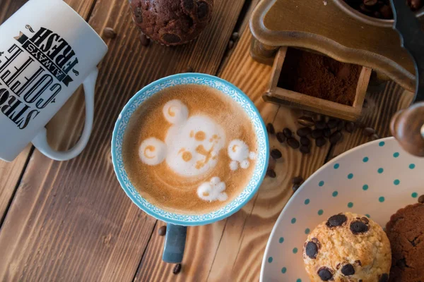 Старая кофемолка и чашка кофе с разбросанными кофейными зёрнами и печеньем на деревянном фоне — стоковое фото