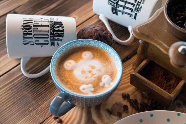 Старая кофемолка и чашка кофе с разбросанными кофейными зёрнами и печеньем на деревянном фоне — стоковое фото