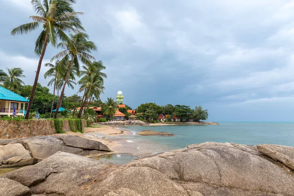 Tropický resort uspořádány v řadě pod palmami na skalnaté pláži na zamračený den — Stock fotografie