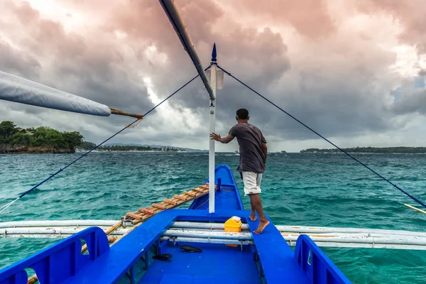 Young filipino man standing at edge of yacht looking at sea. Travelling on old boat at cloudy day. — Stock Photo, Image