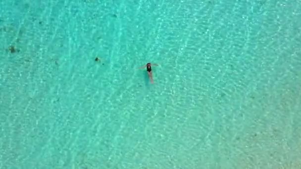 Όμορφη γυναίκα με μαύρο μπικίνι κολυμπάει στη διαφανή, γαλάζια θάλασσα. Εναέρια θέα της λεπτής γυναίκας που επιπλέει στη θάλασσα του γαλάζιου νερού. Η κάμερα κινείται προς τα κάτω. Νήσος μαλκατζένια, Γουάν, Φιλιππίνες. — Αρχείο Βίντεο