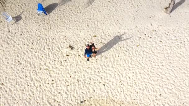 Volar hasta la isla tropical, playa blanca y palmeras con el hombre y la mujer. La cámara sube. Vista aérea 4K — Vídeos de Stock