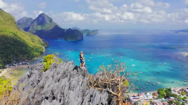 Pareja de excursionistas parados en la cima de una montaña y disfrutando de la vista de la bahía de la laguna azul en El Nido, Palawan, Filipinas. Vista aérea 4K — Vídeos de Stock