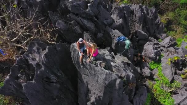 O jovem casal se senta no topo de uma montanha rochosa depois de uma caminhada até o topo. Vista aérea 4K — Vídeo de Stock
