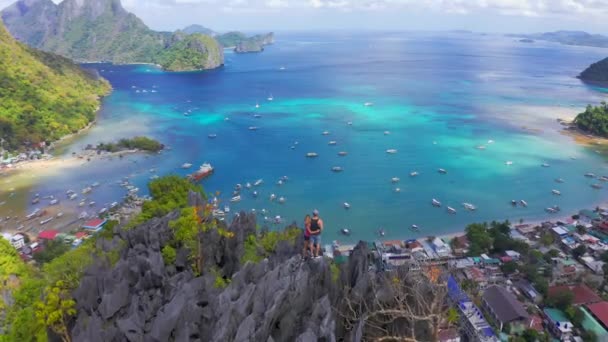 Letí přes turisty, stojící na skalnatém vrcholku hory s výhledem na přístav a modrou vodní lagunu — Stock video