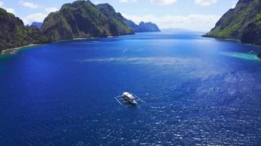Temiz mavi su yüzeyinin üstünde yüzen beyaz geleneksel Filipinli tekne hava drone görünümü. El Nido, Palawan, Filipinler