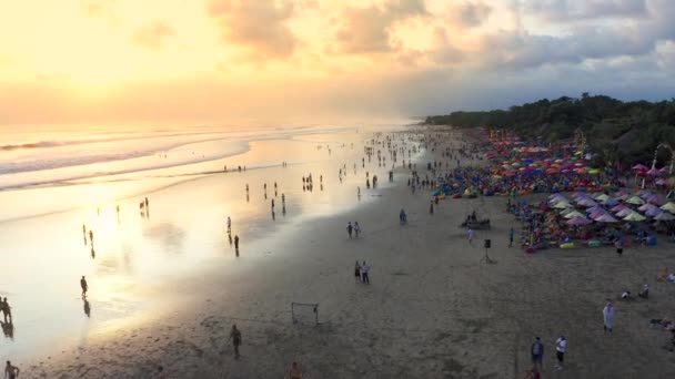 Pessoas sentadas e caminhando na praia e desfrutando da vida de festa em Seminyak Beach ao pôr do sol. 15 de janeiro de 2020: Bali, Indonésia . — Vídeo de Stock