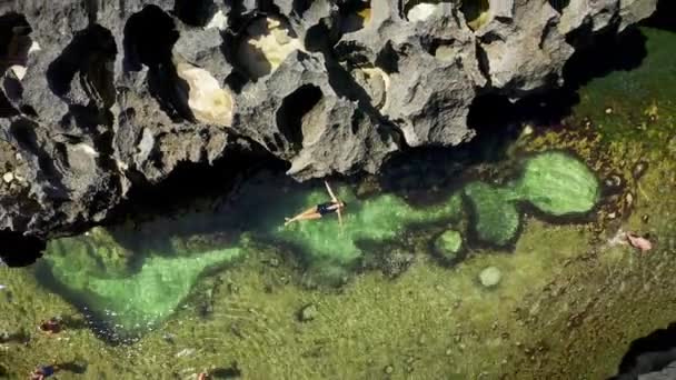 若い美しい女性は、インドネシアのバリ島ヌサペニダ島のブロークンビーチで天然プールエンジェルスビラボンで泳ぎます。空中ビュー｜4K — ストック動画