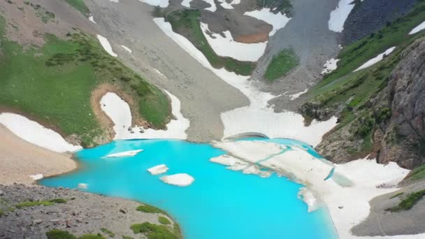 Бирюзовое ледниковое озеро в больших заснеженных горах. Вид с воздуха 4K — стоковое видео