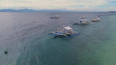 Filipinler 'in Moalboal, Cebu, Filipinler' deki kumlu bir sahil şeridinde, berrak okyanus suyunda yüzen birkaç geleneksel Filipinli teknenin hava manzarası..