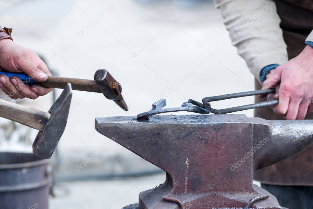 The hands of a blacksmith holding tongs with metal on the anvil