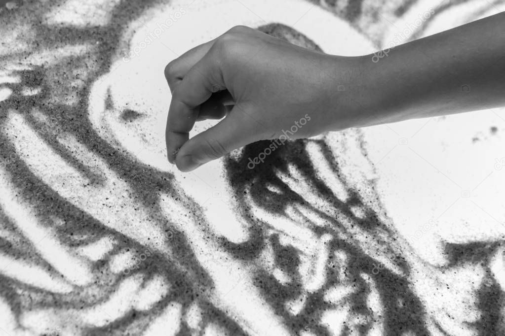 The girl's hand draws with sand on glass