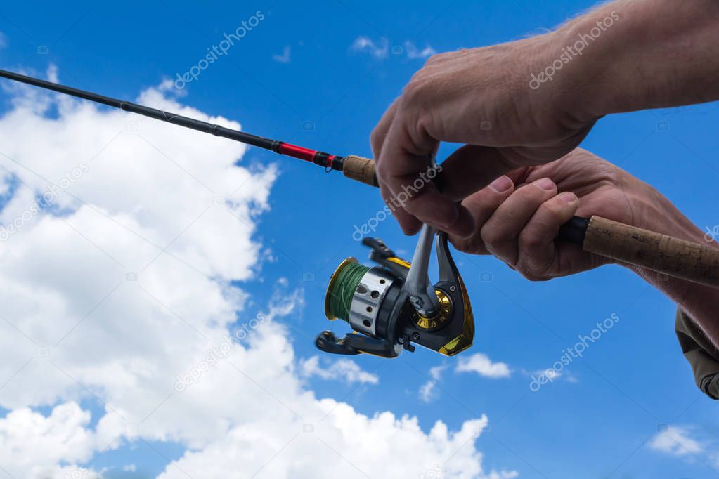 hands of a fisherman with a fishing rod on background sky