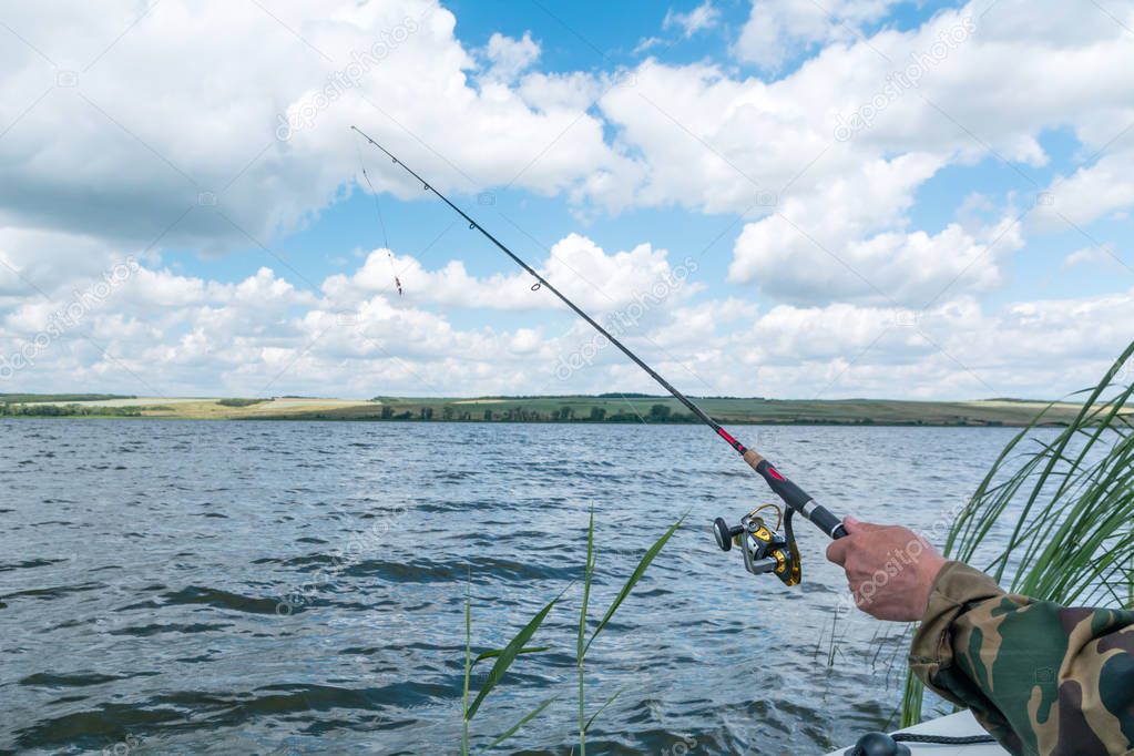 hands of a fisherman with a fishing rod on background of lake and sky