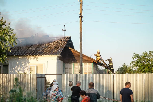 消防队员以紧急情况部的形式出现在屋顶上 扑灭着火的房屋 — 图库照片
