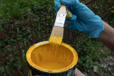 Sarı boyaya batırılmış bir fırça tutan eldivenli el, fazla boya