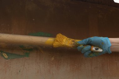 eldivenli el sarı boya batırılmış bir fırça tutar ve bir beni boyar