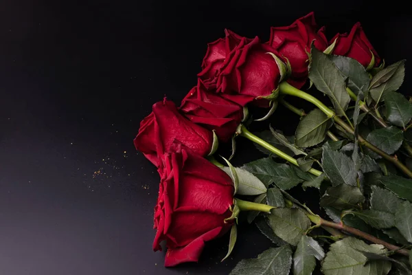 深红色的新鲜玫瑰躺在一个黑暗的房间里的桌子上。a g — 图库照片