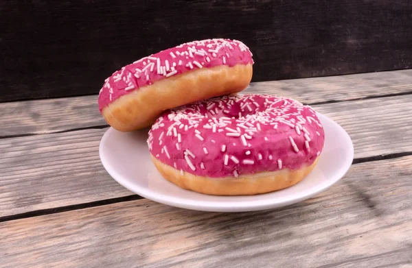 Deux beignets vitrés roses posés dans une petite assiette debout sur un boisé — Photo