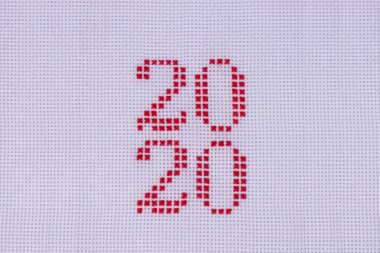 Delikteki beyaz bir bezin üzerindeki kırmızı iplik. İki bin yirmi numara işlemeli. Yakın plan çizilmiş.