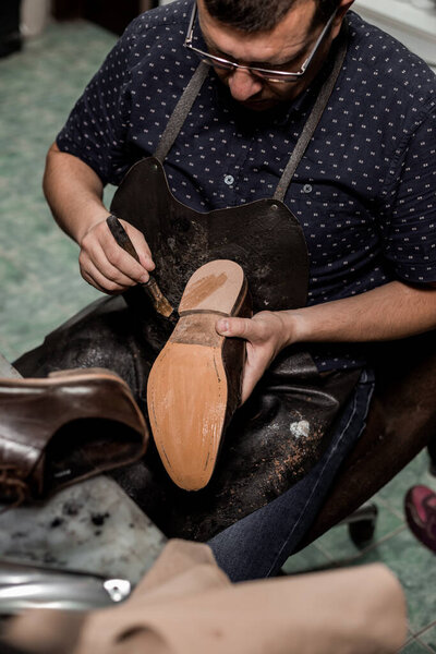 Мужчина сапожник сидит в своем магазине и чинит ботинки, приклеивая подошву клеем. Винтажный вид. 