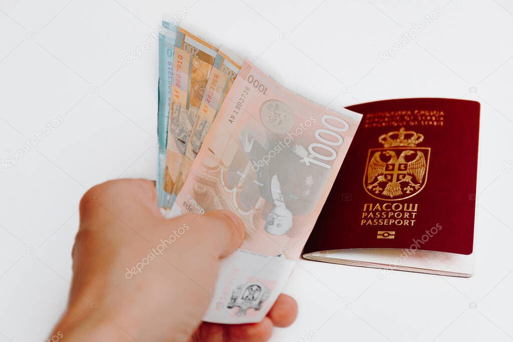 Hand holding Serbian paper money with out of focus Serbian passport lying in background