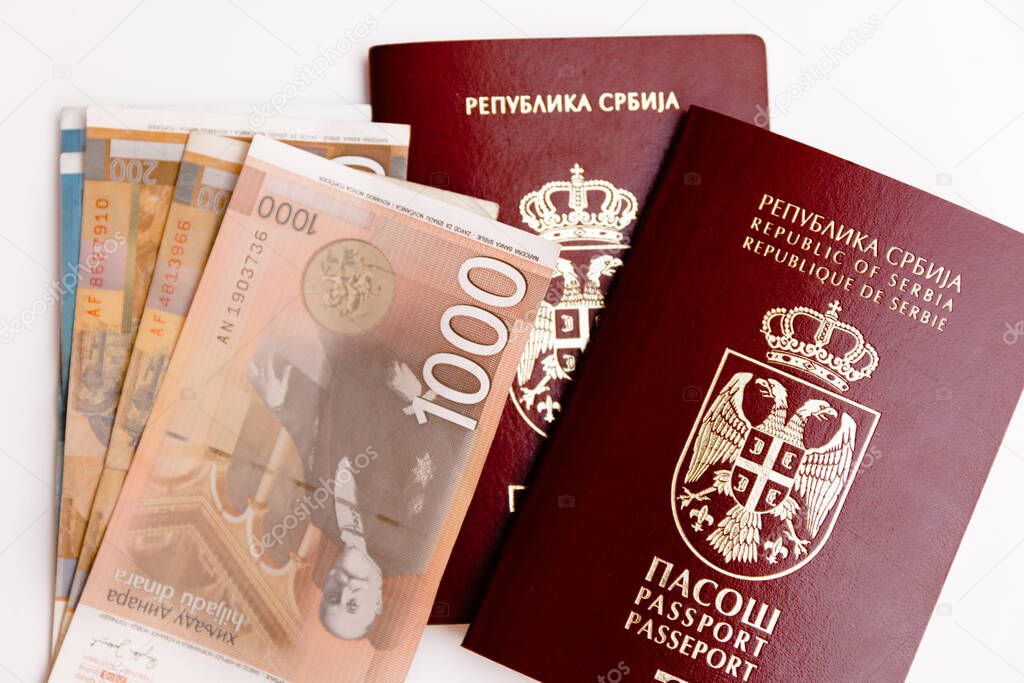Two Serbian biometric passports with pile of Serbian money around, isolated on white background