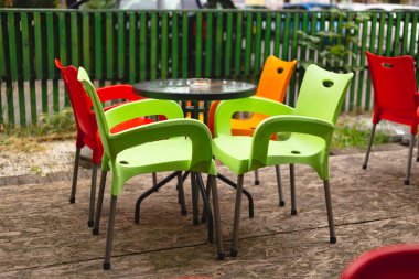 Bulutlu ve yağmurlu bir günde boş masa ve kafe terasında sandalyeler. Çok canlı renkler ve renkli bir dış görünüş.. 