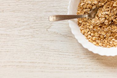 Tahta masadaki bir kase kuru yulaf. Kase görüntünün sağ üst köşesinde..