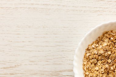 Tahta masadaki bir kase kuru yulaf. Kase görüntünün sağ alt köşesinde.. 