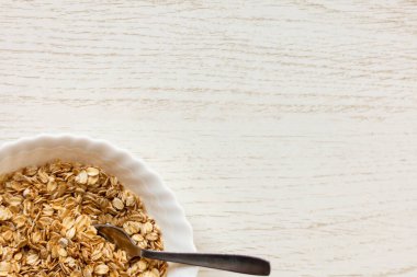 Tahta masadaki bir kase kuru yulaf. Kase görüntünün sol alt köşesinde.. 