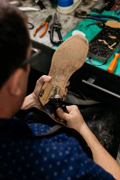Male shoemaker using pliers to remove shoe sole. Cobbler at work.