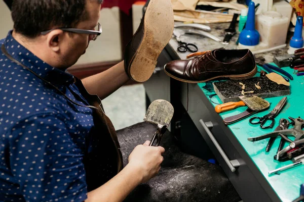 Male shoemaker using pliers to remove shoe sole. Cobbler at work.