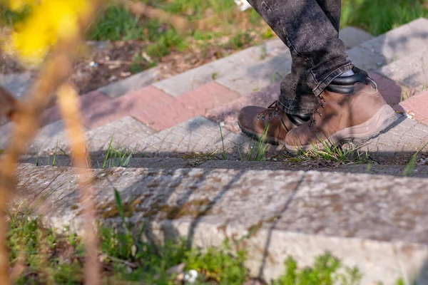 Kahverengi kışlık ayakkabılı ve kot pantolonlu bir adam merdivenlerden iniyor, yakın çekim, sadece bacakları görünüyor..