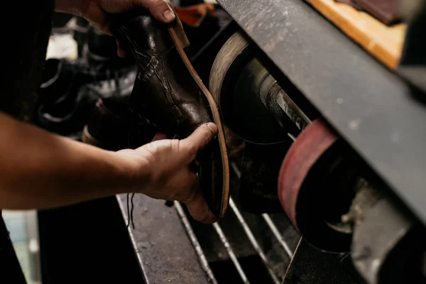 Male shoemaker repairing sole of shoe on grinding machine. Cobbler at work.