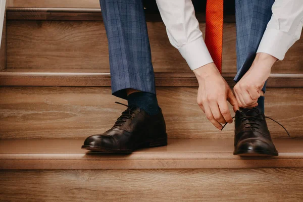 Businessman tying a shoes while sitting on wooden stairs at home, getting ready for work.