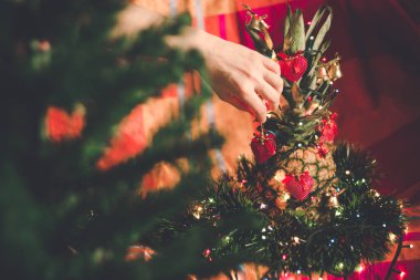 Alternatif Crhistmas ağacı olarak ananas dekore eden kadın. Süsleri ve renkli arka planda Noel ışıkları.